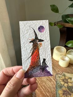 a hand holding up a card with an image of a witch on it