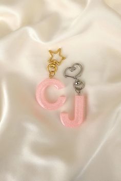 two charms with the letter j on them are laying on a white satin material background