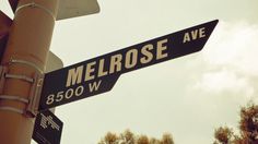 two street signs that are on top of a traffic light pole with trees in the background