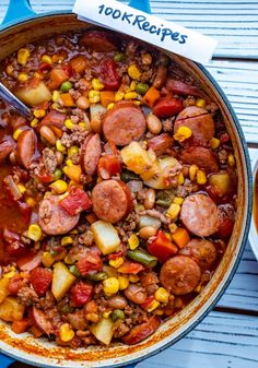 a large pot filled with lots of food on top of a wooden table next to a spoon