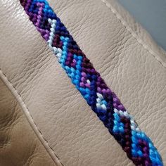 a close up of a braided wristband on a brown leather bag with blue, purple and white beads