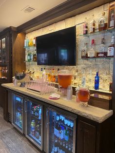 a bar with many bottles and glasses on the counter, in front of a flat screen tv