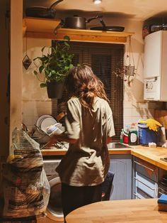 a woman standing in a kitchen next to a potted plant