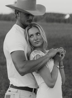 a man and woman standing next to each other in a field wearing cowboy hats on their heads