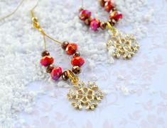 two red and gold beaded earrings laying on top of white snow covered tablecloth