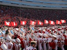 a marching band with red and white uniforms in front of a stadium full of people