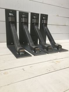 three black metal stands on top of a wooden floor next to a white wall with wood planks