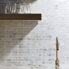 a kitchen with marble counter tops and white brick backsplashing, along with two wine glasses on the shelf