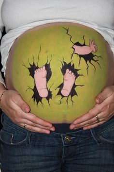 a pregnant woman holding her belly in front of her stomach with two feet painted on it