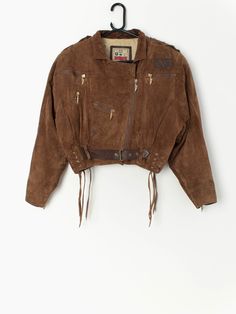 "Vintage cropped tan leather jacket with belt by Leather Sound. The jacket is genuine leather that is super soft to touch, has a cotton lining and is fastened at the front with a gold zip with a \"LS engraved\", a brown leather belt and drawstrings on the hem. The jacket also has three functional pockets with shiny gold zips and one non-functional pocket. Made in the UK from a heavyweight soft leather, with a cotton lining. Made circa 1980. Our recommended size: Small to medium Label Says: Small Leather Cropped Biker Jacket For Fall, Fall Cropped Leather Biker Jacket, Cropped Leather Biker Jacket For Fall, Spring Brown Belted Leather Jacket, Fall Cropped Belted Jacket, Brown Leather Long Sleeve Cropped Jacket, Brown Leather Cropped Jacket With Long Sleeves, Leather Jacket With Belt, Tan Leather Jacket