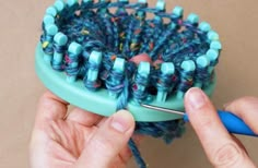 someone is holding a blue and green hair brush with yarn on it, while another person holds a pair of scissors in front of the brush