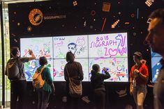 people are standing in front of a large screen with images on it and writing on it