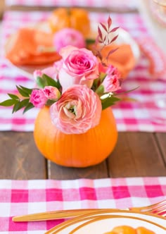 an orange vase filled with pink flowers sitting on top of a table next to plates and utensils