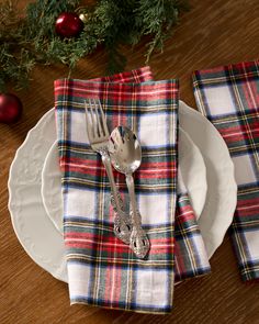 a plaid napkin and silverware on a white plate with christmas decorations in the background