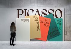 a woman standing in front of a sign that reads picasso and has five different colored books stacked on it