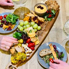 two people are serving themselves food on a long wooden platter with grapes and bread