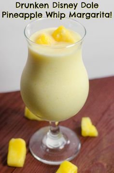 a glass filled with pineapple whip margarita on top of a wooden table