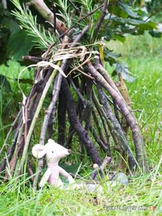 a teddy bear sitting in the grass next to a pile of sticks and branches that have been placed together