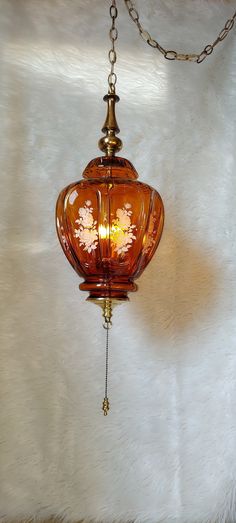 an orange glass light hanging from a chain on a white furnishce wall behind it