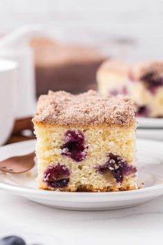 a slice of blueberry coffee cake on a plate with a cup of coffee in the background