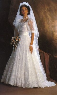 a woman in a wedding dress posing for a photo with her veil pulled back over her shoulder