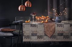 a table with candles and fruit on it in front of a black wall, next to two chairs