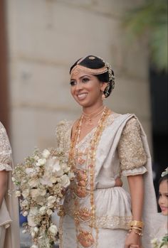 a woman in a white dress holding a bouquet and smiling at the camera while standing next to another woman