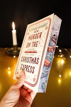 a person holding up a book in front of a lit candle