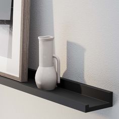 a white vase sitting on top of a black shelf next to a framed photograph and a wooden frame