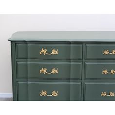 a large green dresser with gold handles and drawers on it's sides, in front of a white wall