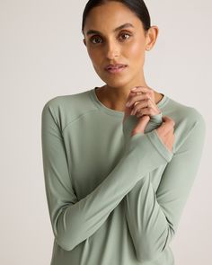 a woman in a green top poses for the camera with her hands on her chest