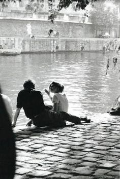 two people sitting on the ground next to a body of water