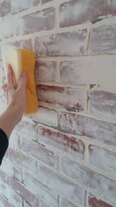 a hand holding a piece of cheese up to a brick wall that has been painted white