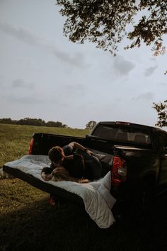 two people laying in the back of a pick up truck on top of a field