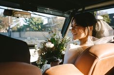 a bride sitting in the back seat of a car holding a bouquet of white flowers