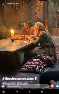 two people sitting at a table with a lit candle in front of them on the floor