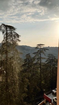 the sun shines through the clouds over some trees and mountains in the distance, while cars are parked on the road