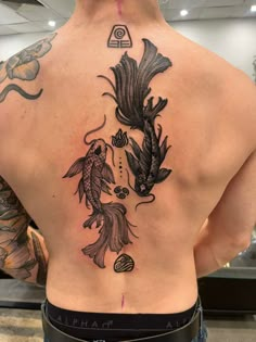 the back of a man's tattoo with fish and flowers on his upper back