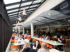 many people are sitting at tables in an indoor restaurant with orange chairs and large windows