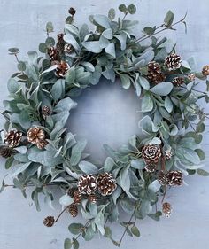 a wreath with pine cones, eucalyptus leaves and greenery on a white wall background