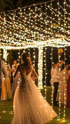 a bride and groom walking through the grass at night with fairy lights all around them