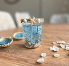 a jar filled with sand and shells on top of a wooden table