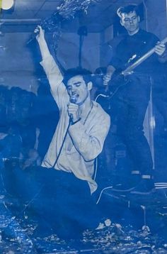 an old photo of two young men singing into microphones while another man plays guitar in the background