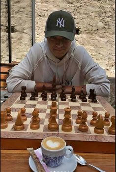 a man sitting at a table with a chess board and cup of coffee in front of him