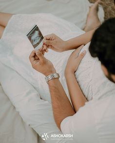 a man and woman laying on top of a bed next to each other holding an electronic device