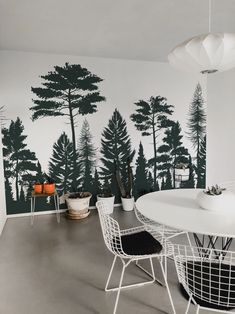 a white table and chairs in front of a wall with trees painted on the walls