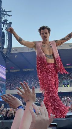 a man in a pink dress standing on top of a stage with his arms outstretched