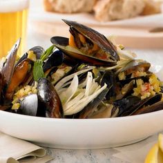 a white bowl filled with mussels on top of a table next to lemon wedges