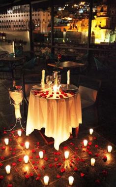 a table with candles and flowers on it in front of a large window at night