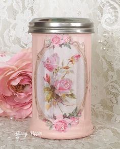 a pink canister sitting on top of a white lace covered tablecloth next to a pink flower